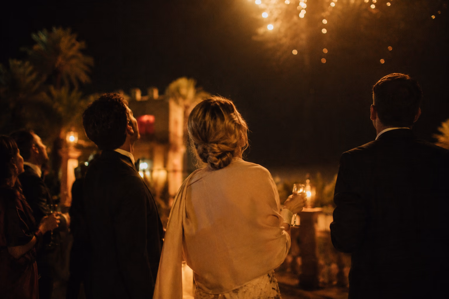 Invités en tenue de soirée, vus de dos, le regard levé vers un bouquet doré